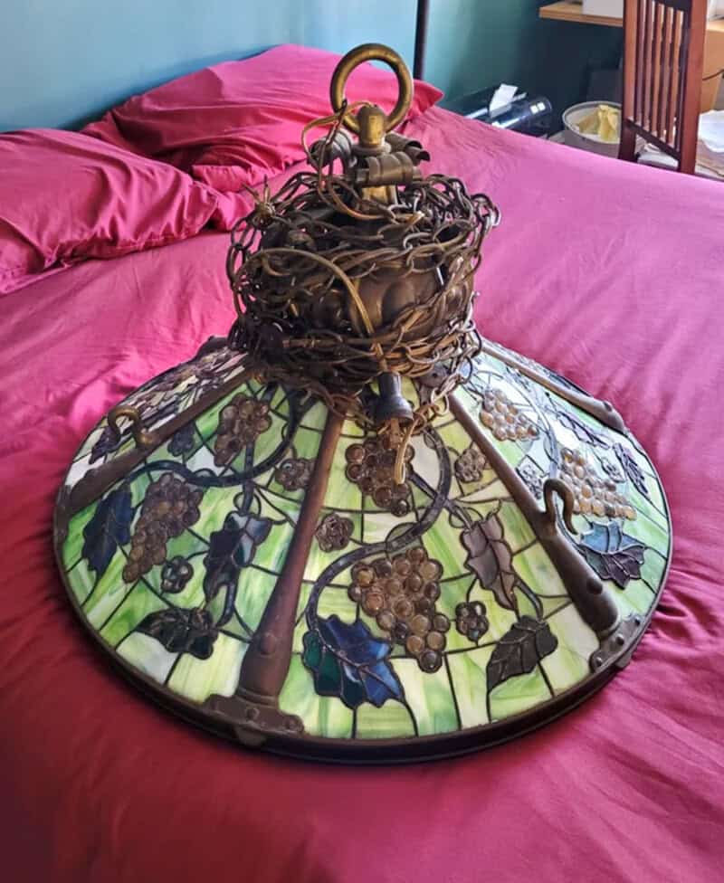 Vintage stained glass lamp with grapevine design, tangled wires on top, on a pink bed.