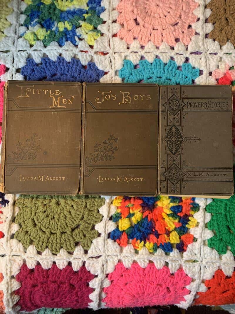 Three vintage books titled 'Little Men,' 'Jo's Boys,' and 'Proverb Stories' on a colorful crochet af.