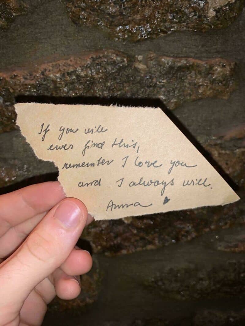Hand holding a note against a stone wall with a heartfelt message.