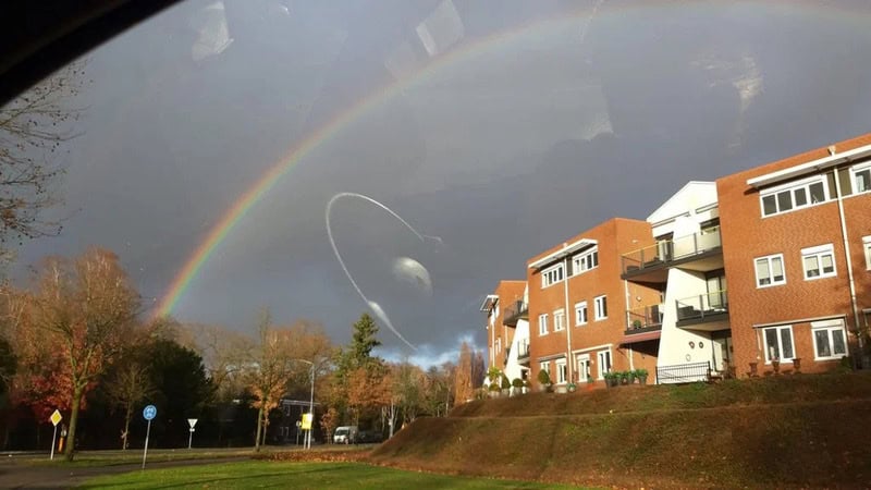 Rainbow over buildings and trees with a planet and spaceship in the sky.