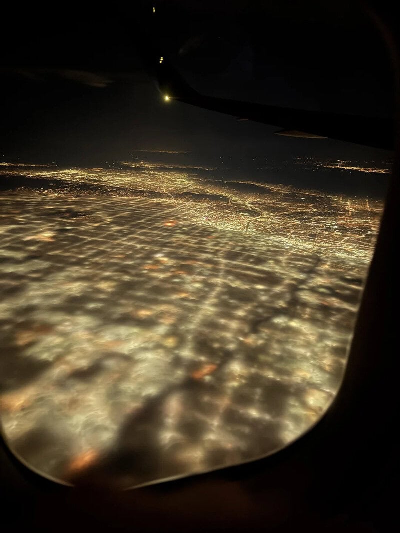 Nighttime view of city lights from an airplane window with clouds and stars.