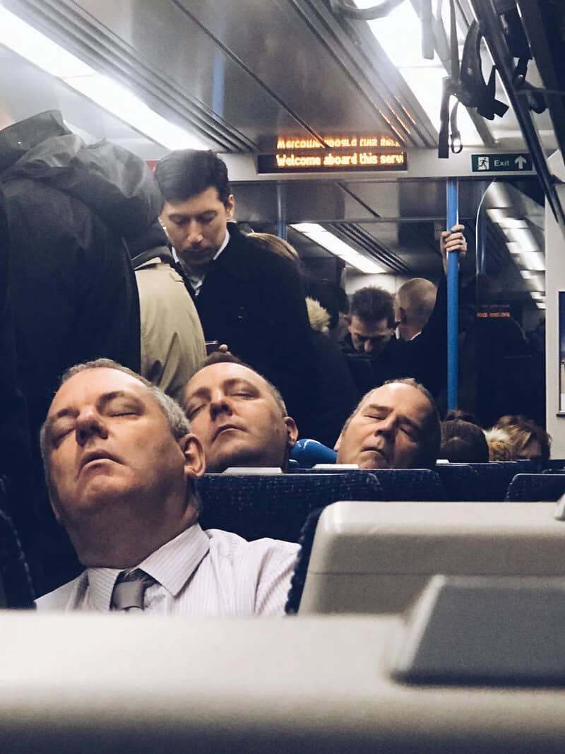 Three men sleeping on a bus with a crowded background and a digital sign.