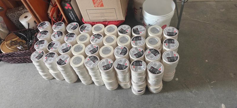 Stack of white plastic buckets with black and red labels on a concrete floor.