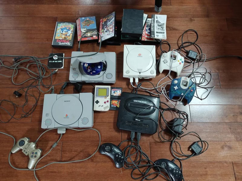 Various gaming consoles, controllers, and video games on a wooden floor.