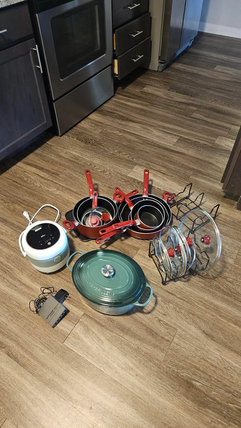 Various kitchen items and cookware on a wooden floor near cabinets and a stove.