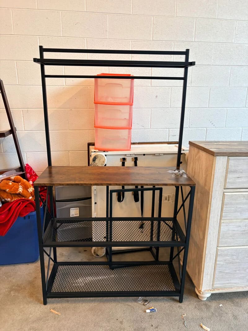 Empty black metal shelving unit with a red plastic storage container on top, against a white brick c.