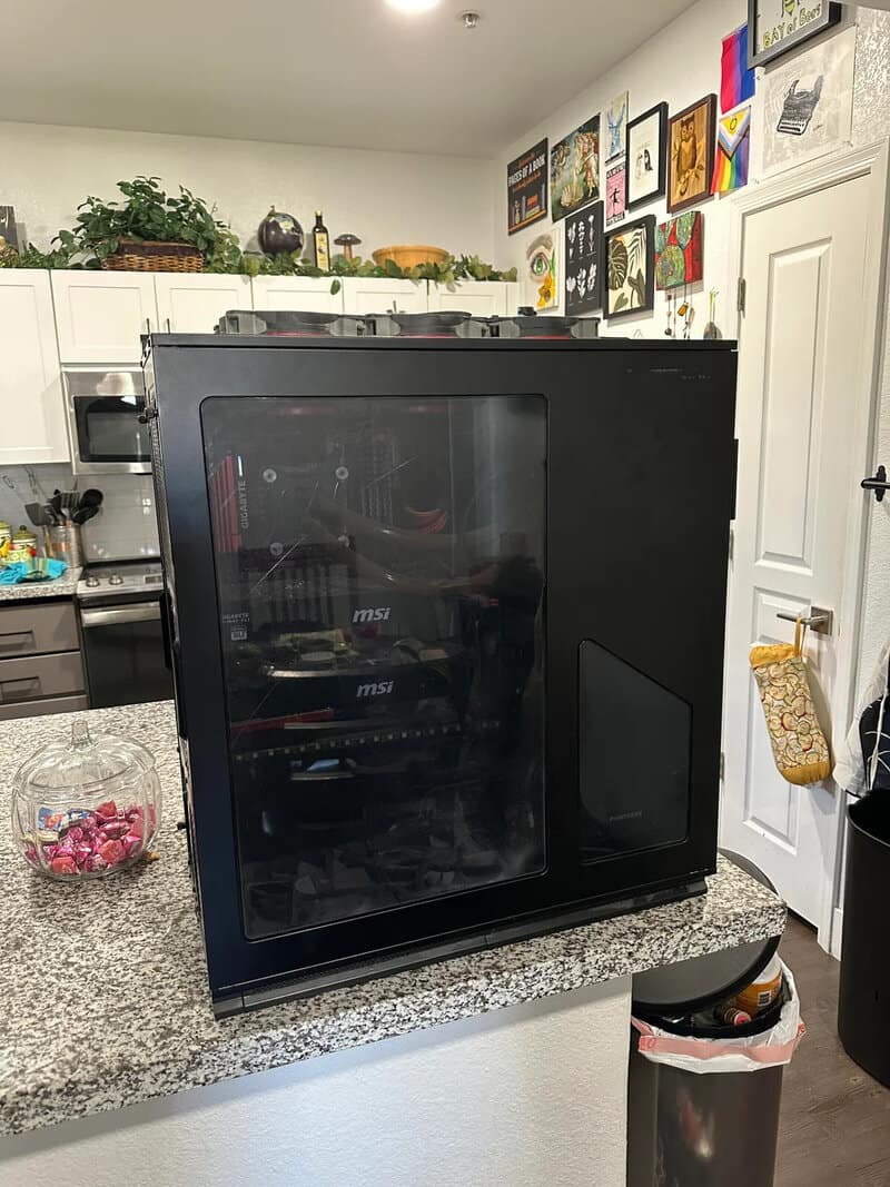 Black computer case with glass side panel on kitchen counter in a home.