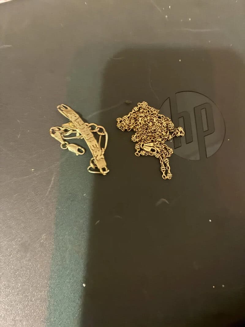 Two gold chains and a gold bracelet on a black surface with a logo.