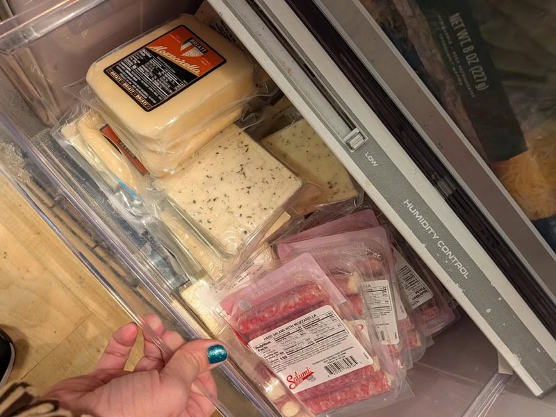 Cheese and meat packages inside a refrigerator door.