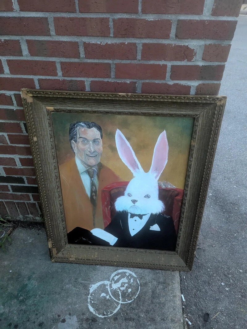 Framed painting of a man and a rabbit in tuxedo, leaning against a brick wall.
