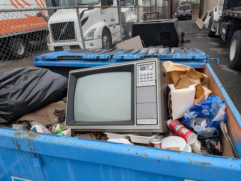 Old microwave in a dumpster filled with trash and debris.