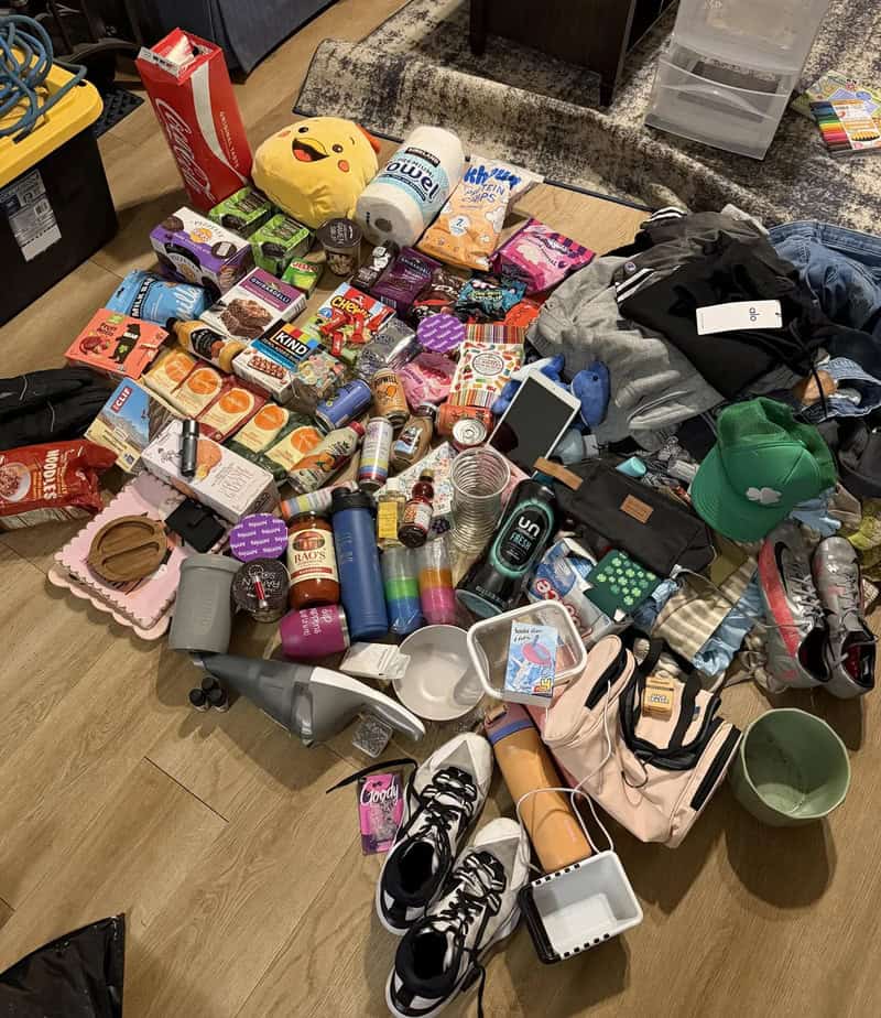 Cluttered table with snacks, clothes, shoes, and personal items in a room.