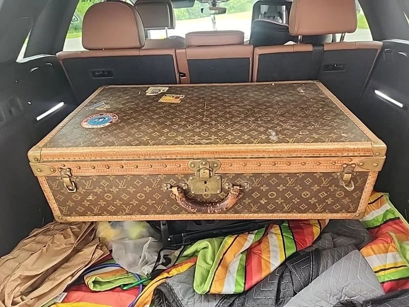 Vintage Louis Vuitton trunk in the back of a car with colorful blankets and bags.