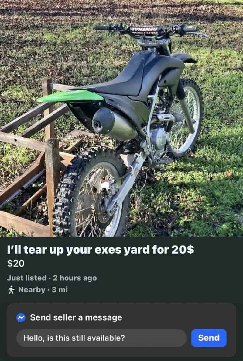 Green and black dirt bike on grass with a wooden fence nearby.