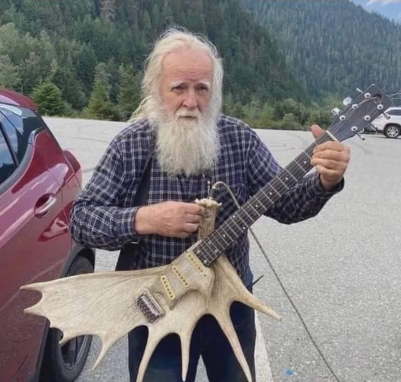 Old man with long white beard holding a guitar with a moose antler body.