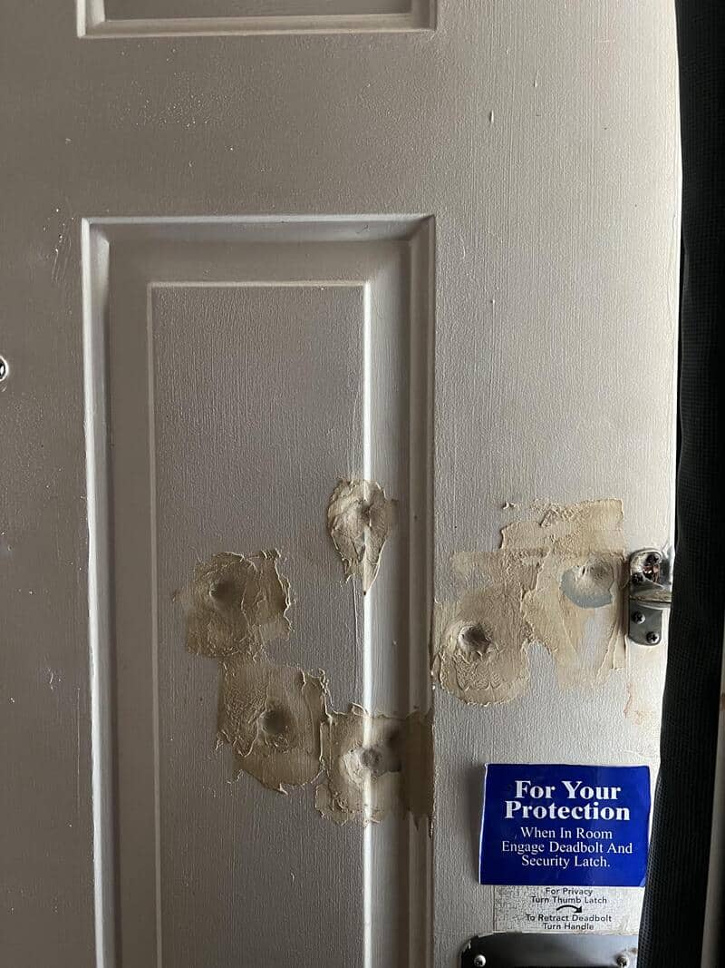 Damaged door with multiple holes and a security sticker.