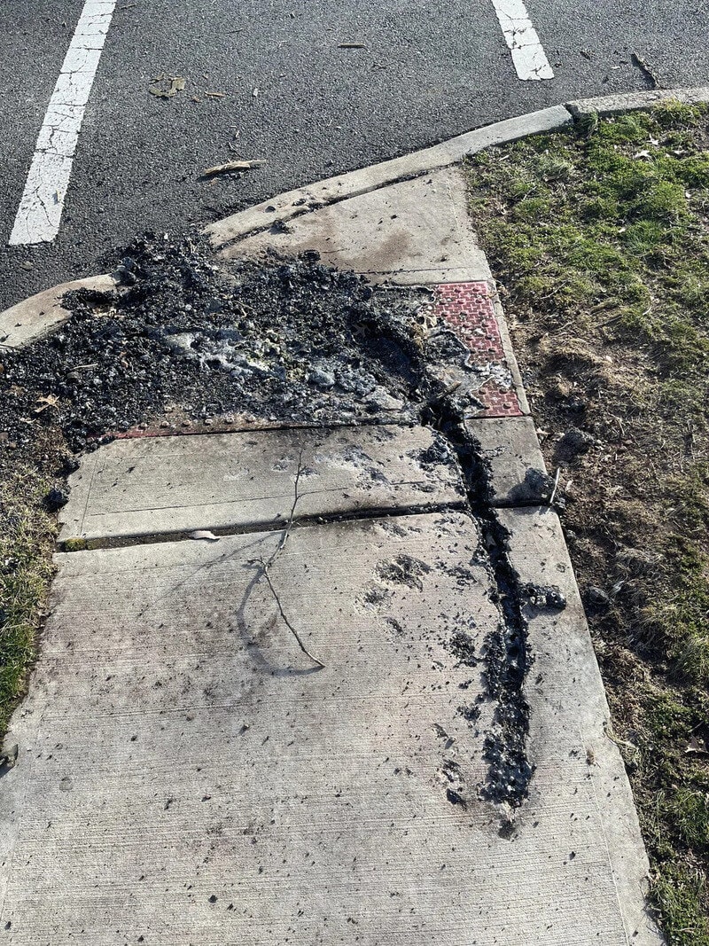 Damaged sidewalk with burnt and broken asphalt near parking lot.