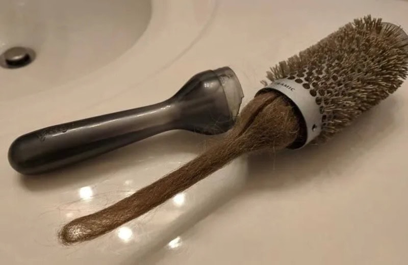 A hairbrush with a long, brown hair extending from it on a bathroom sink.