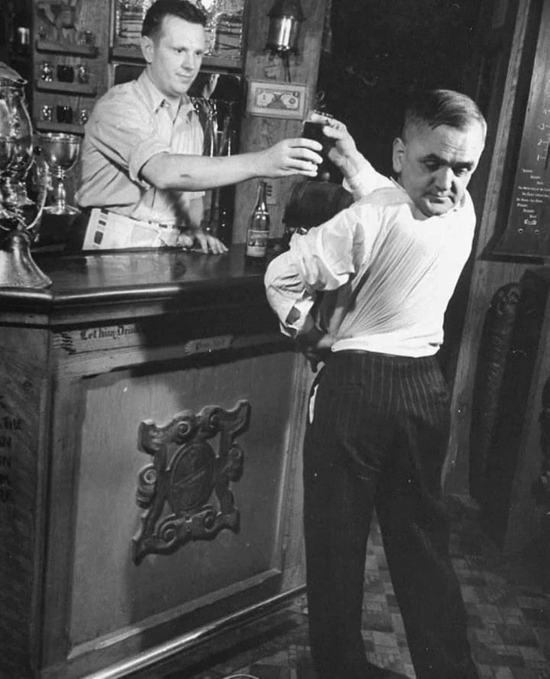 Man in white shirt and dark pants gets hit with drink from bartender.
