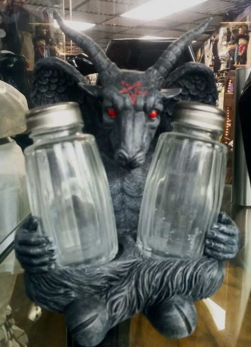 Goat-like demon statue holding two glass jars with red eyes and a pentagram on its forehead.