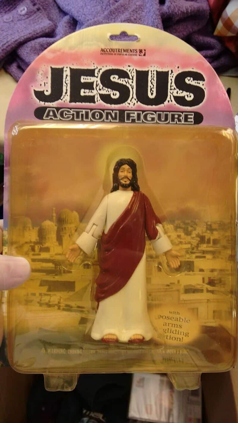 Jesus action figure in white robes with red sash, gold background cityscape package.