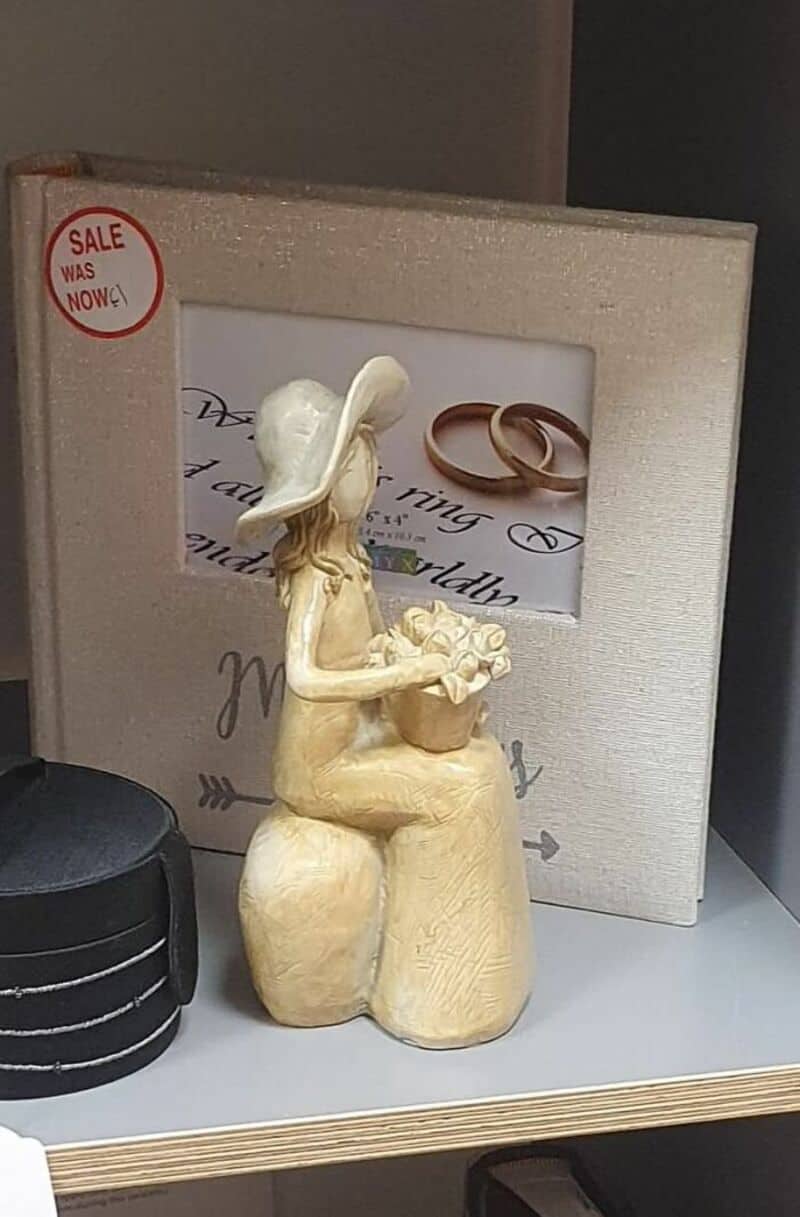 Ivory figurine of a seated woman wearing a hat holding a small bouquet, displayed on a shelf with a.