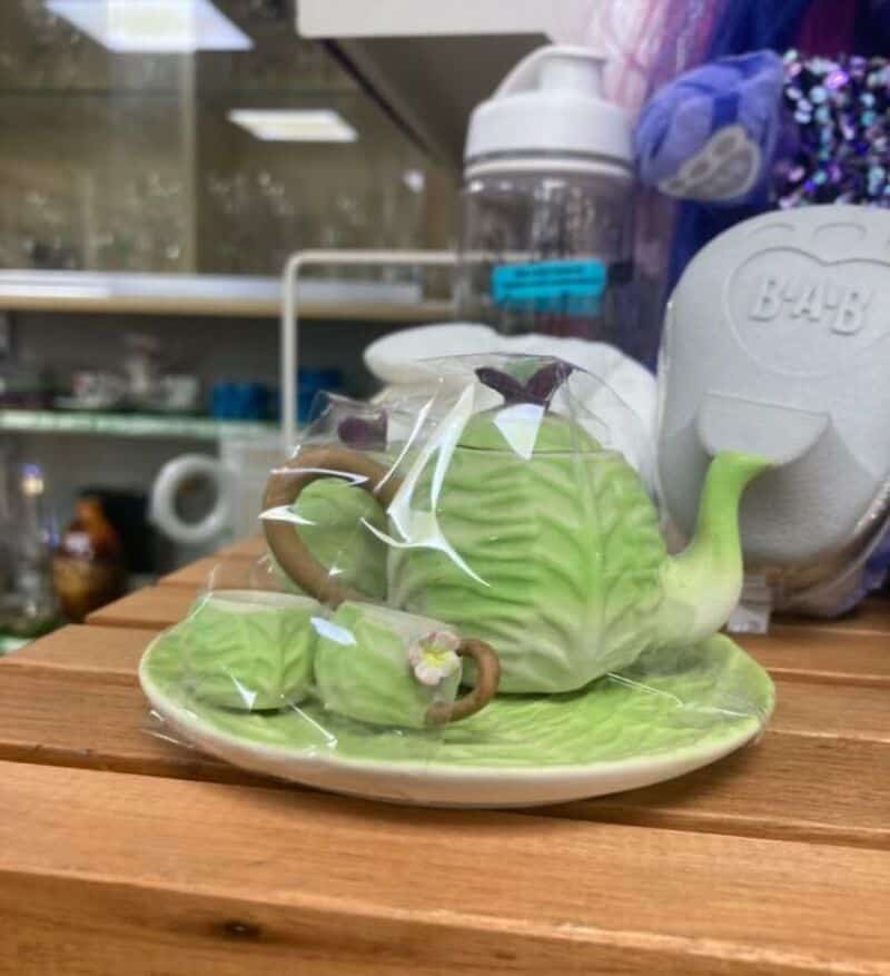 Green teapot and cup set on a plate, wrapped in plastic, in a shop display.