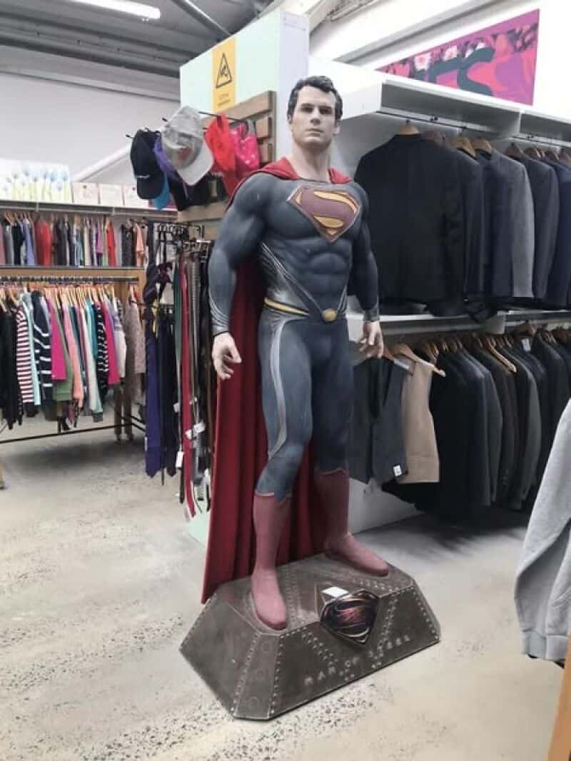Superman statue in a thrift store aisle with clothes racks in background.