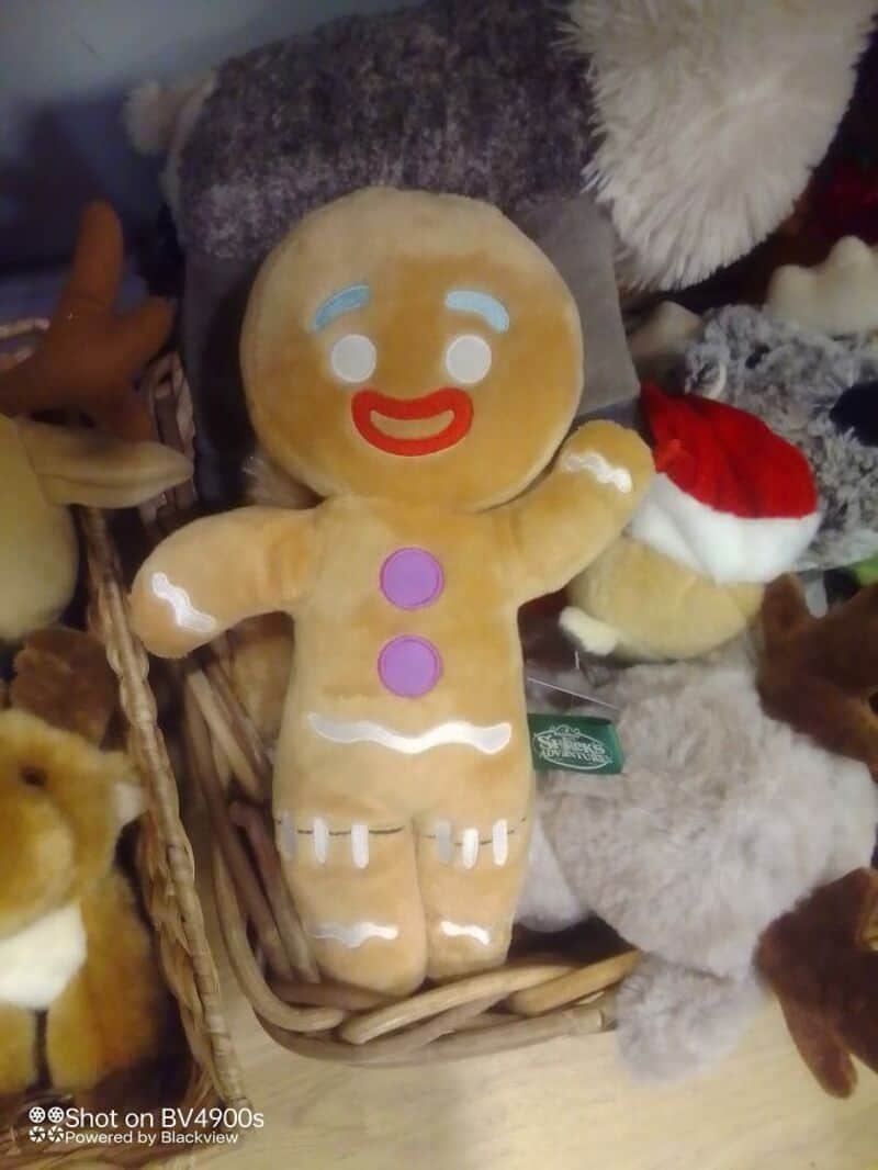 Gingerbread-themed plush toy with blue eyes, red smile, two purple buttons, white icing details, and.