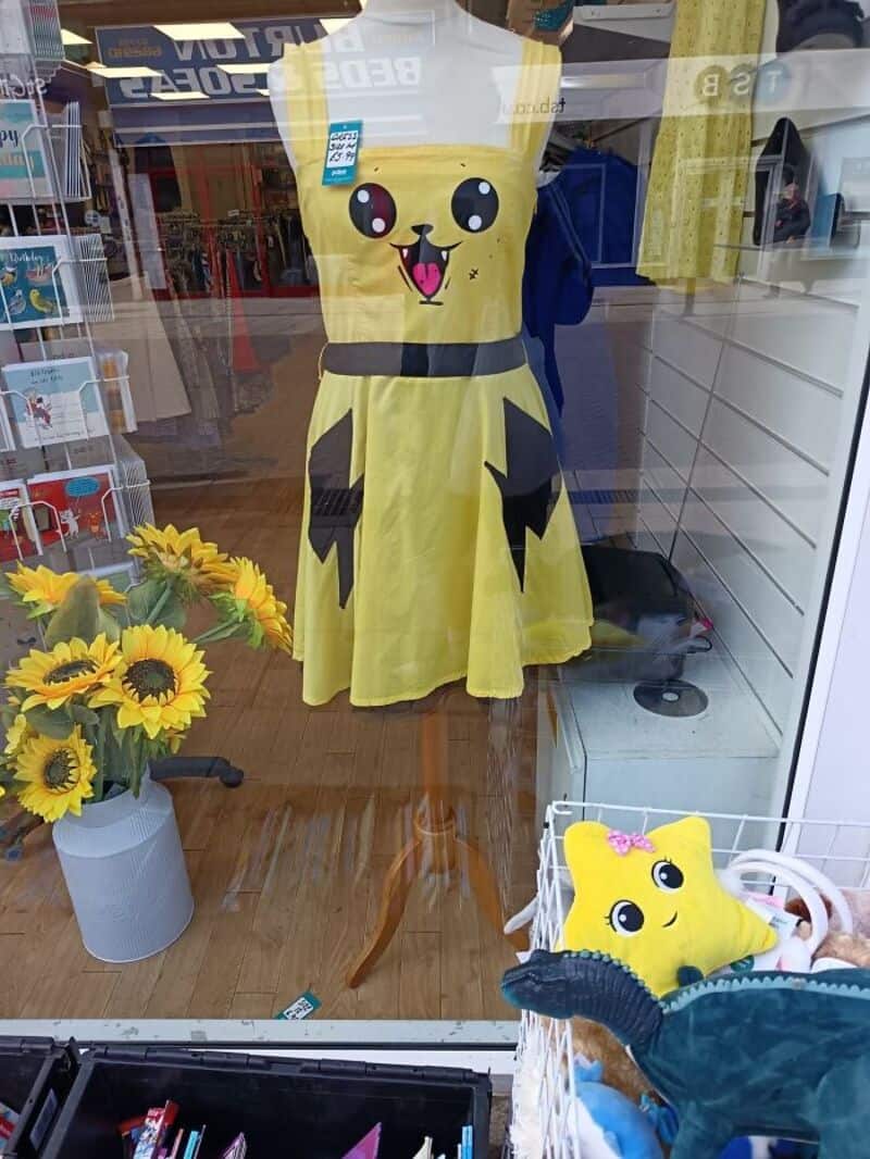 Yellow Pikachu-inspired dress on mannequin in shop window, with sunflower bouquet nearby.