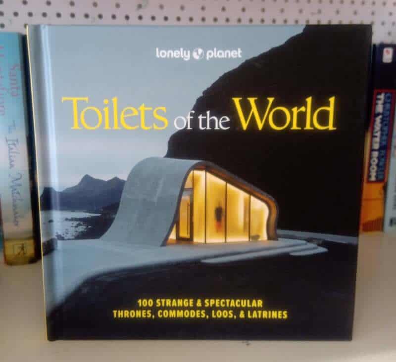 Toilets of the World book cover on a shelf with alpine background.
