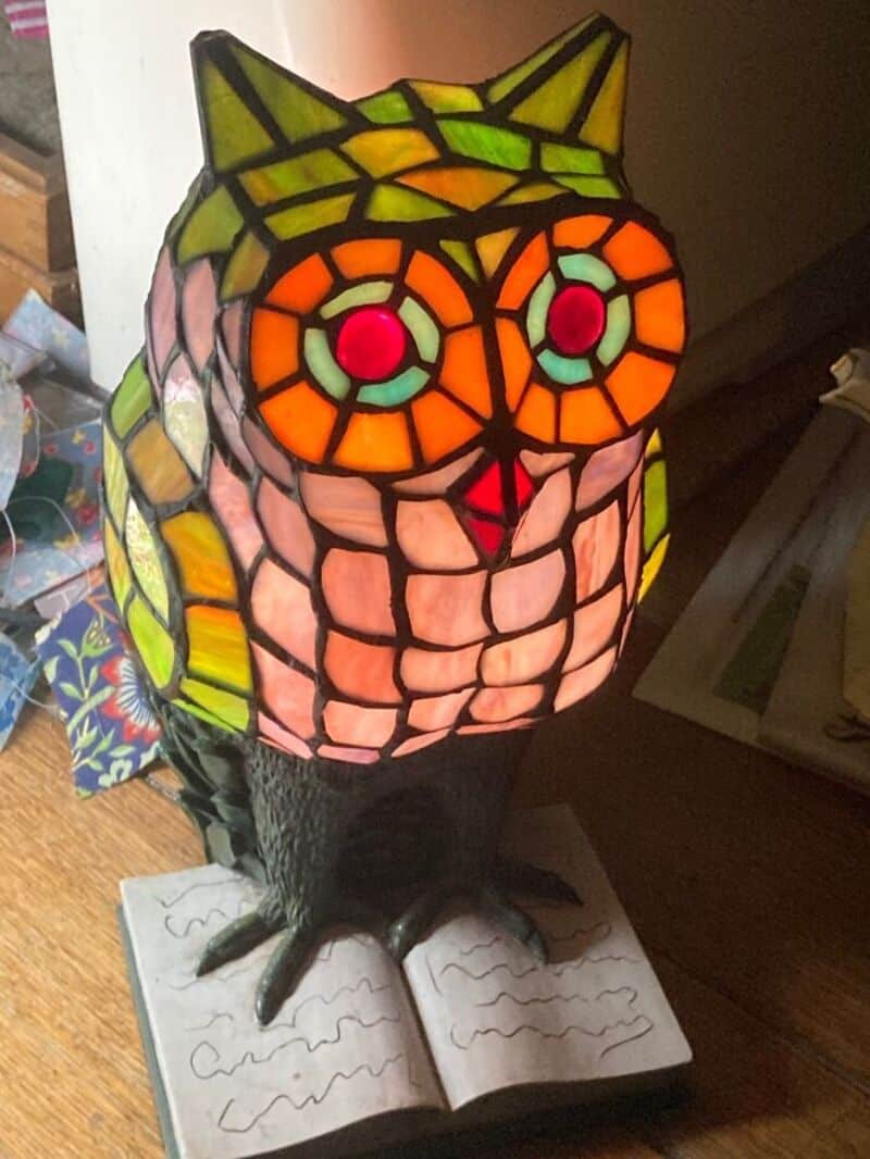 Colorful stained glass owl lamp with geometric pattern, perched on a book, indoors.