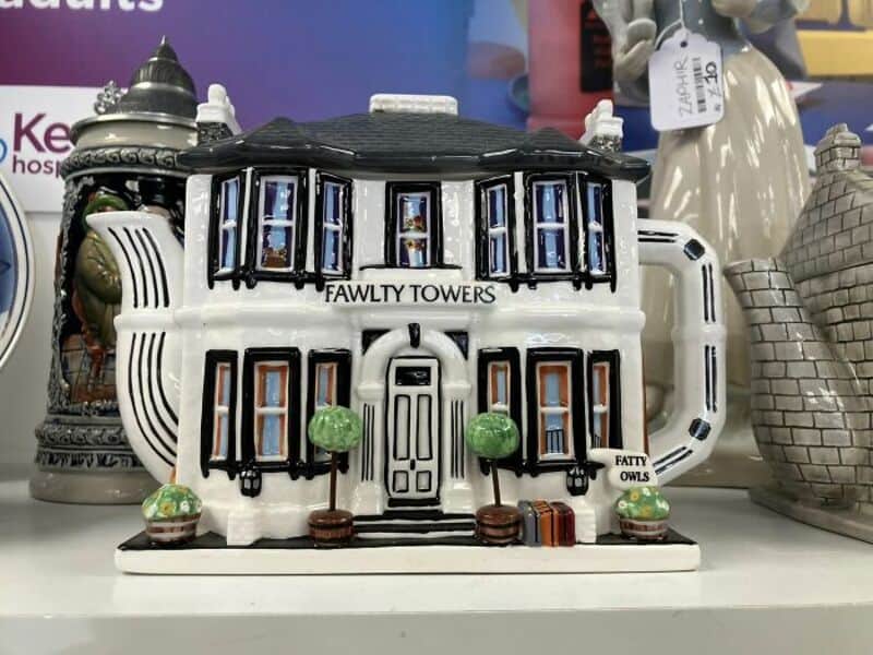 Fawlty Towers ceramic miniature hotel with black roof, white walls and green trees in front.