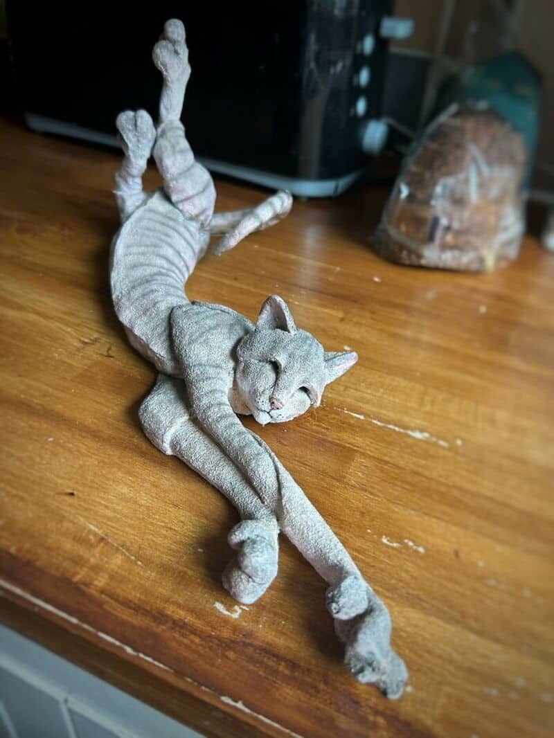 A gray cat sculpture stretched on a wooden surface with its front legs extended.