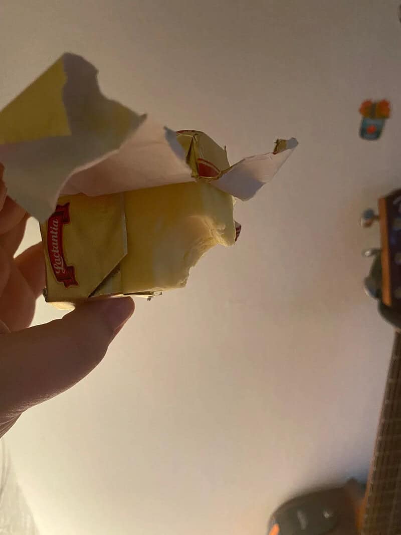Hand holding a torn piece of paper with a small red and white object inside.