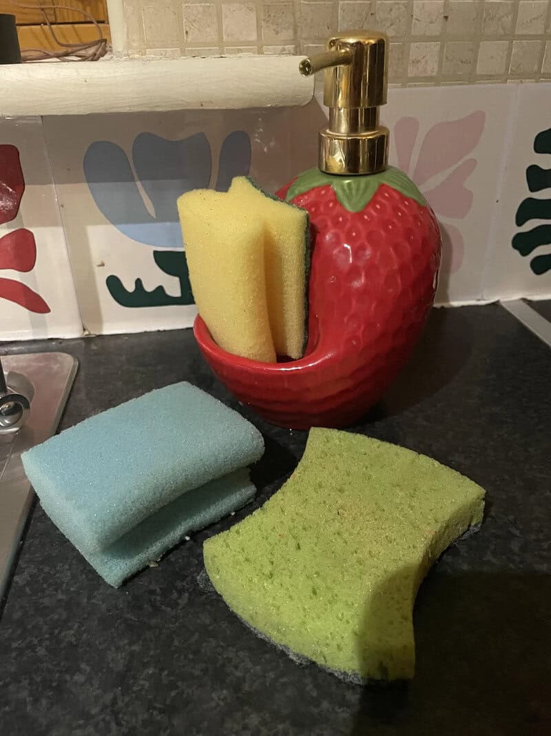 Strawberry-shaped soap dispenser with sponges and cleaning cloths on a kitchen counter.