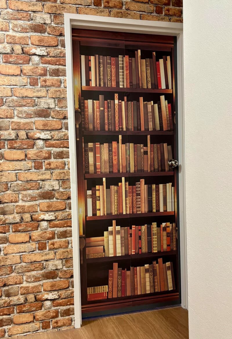 Bookcase door with shelves of books, set against a brick wall.